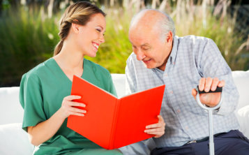 smiling caregiver reading a book with the elderly man