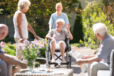 nurse pushing a wheelchair and her patient waving on the other people around